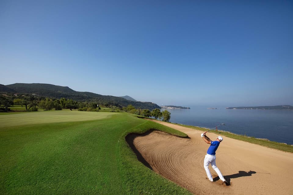A golfer splashes out of a bunker on the Bay Course at Costa Navarino